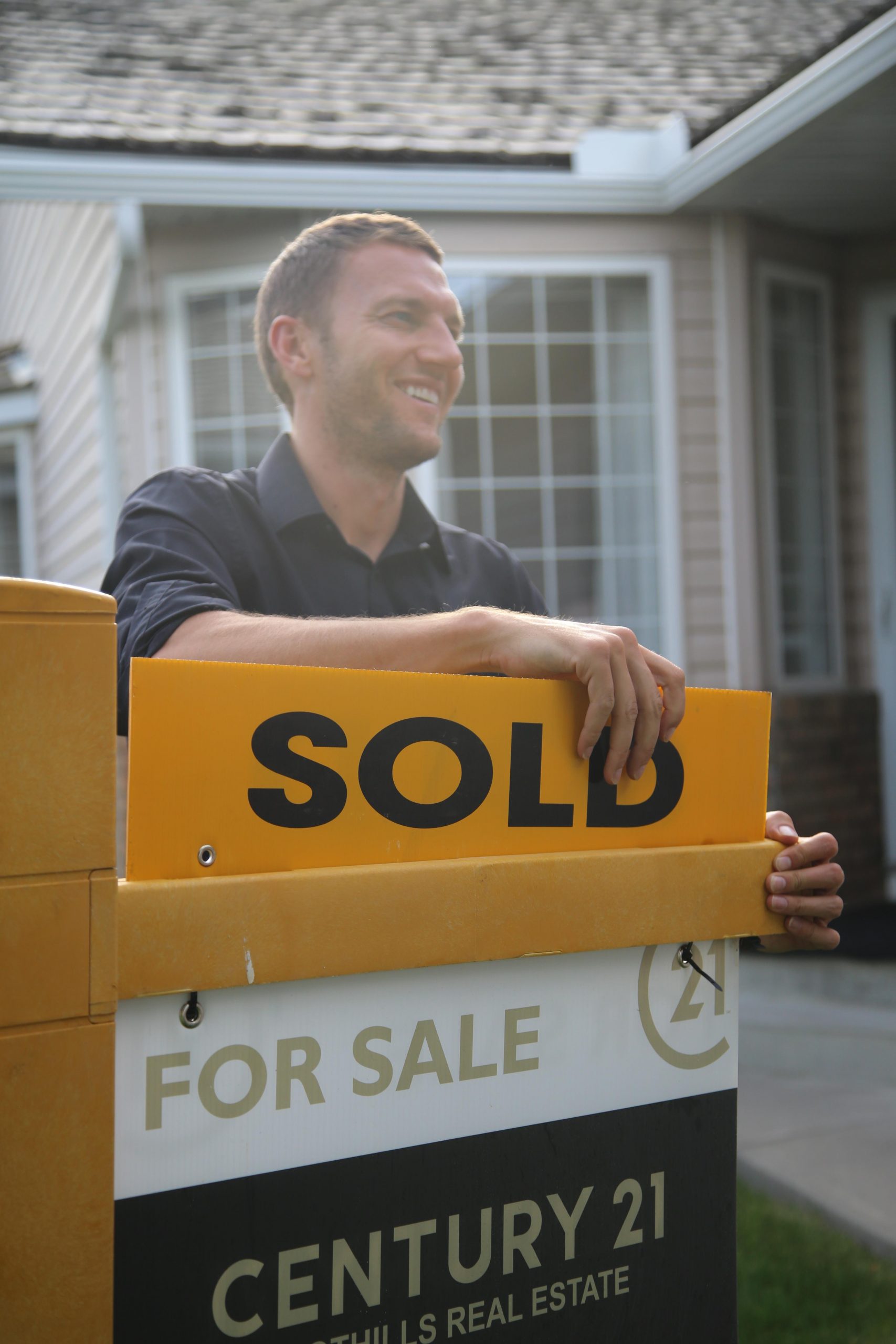 High River Realtor, John Seacrist holding a sold sign in front of a house in High River.
